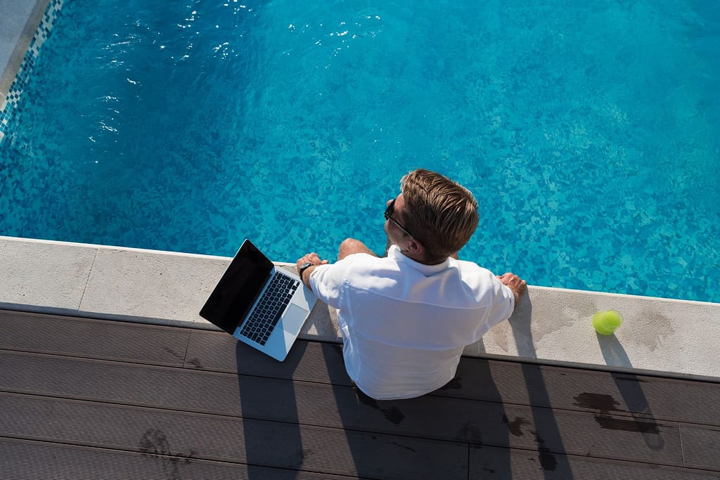 Unternehmer sitzt am Pool und arbeitet am Laptop