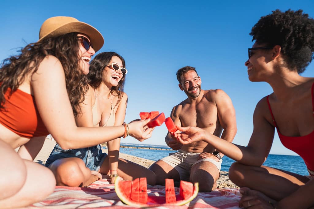 Vier Freunde essen eine Wassermelone am Strand