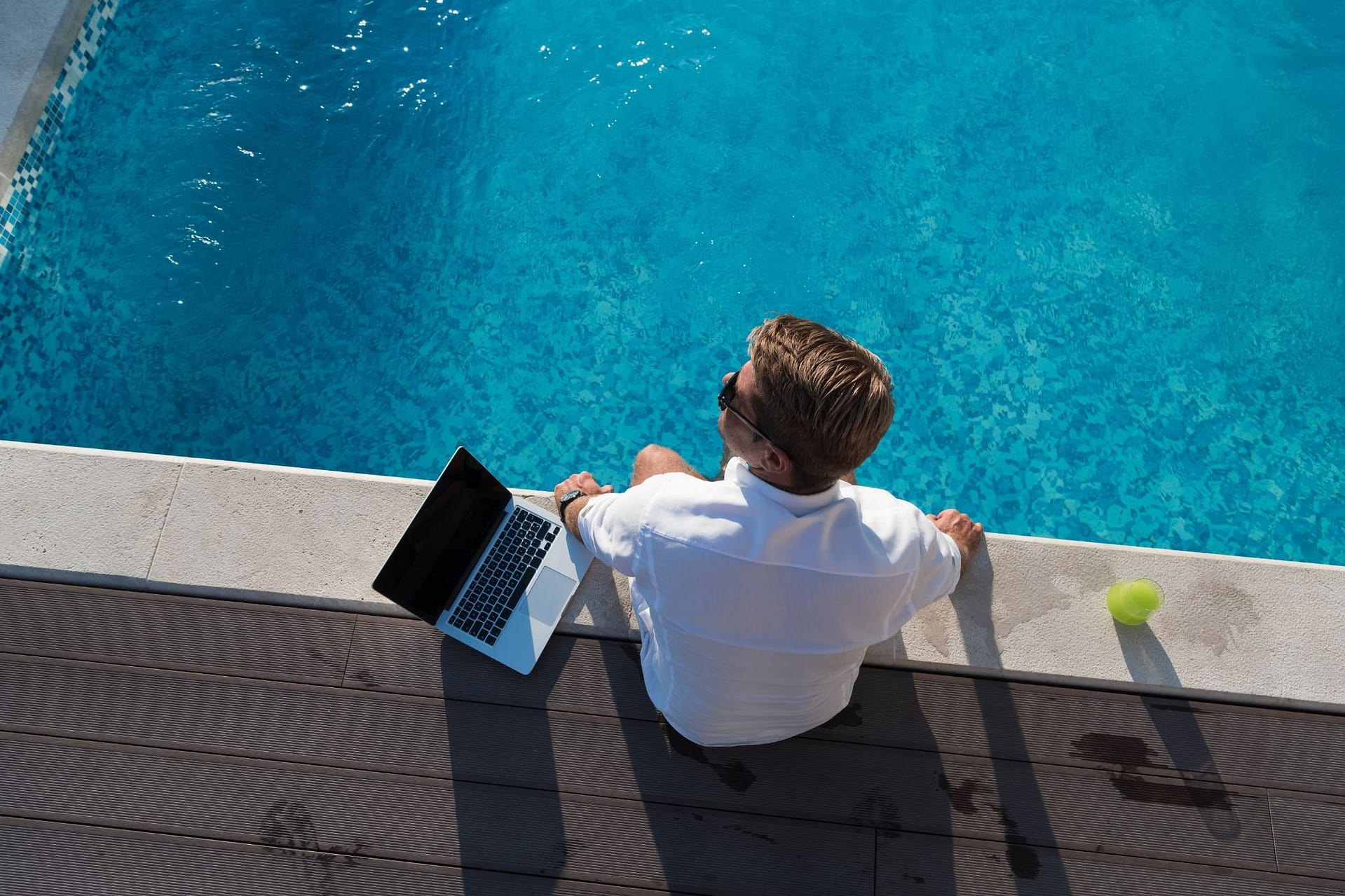 Unternehmer sitzt am Pool und arbeitet am Laptop