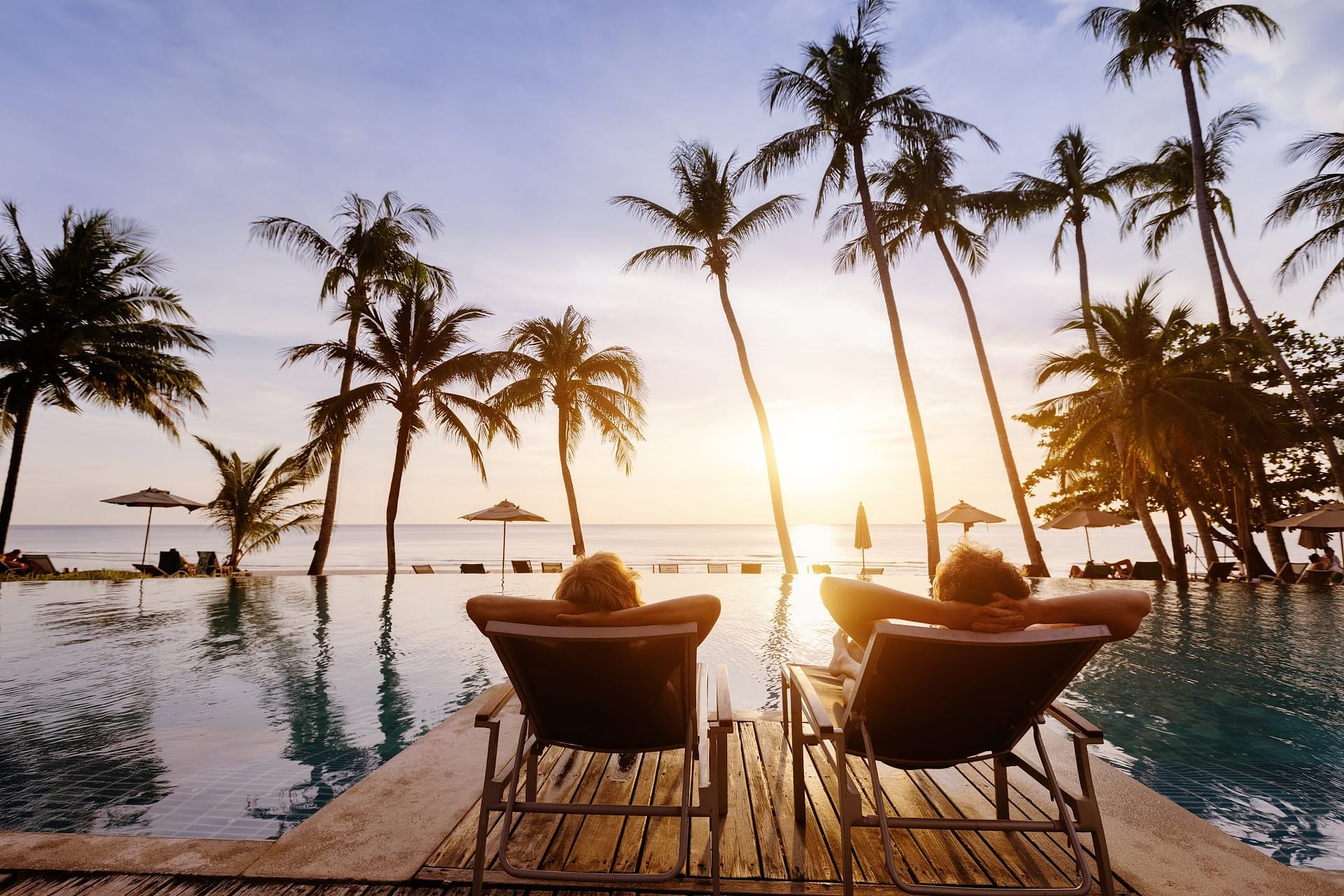 Ein Paar entspannt bei Sonnenuntergang auf Liegestühlen am Pool mit Blick auf das Meer