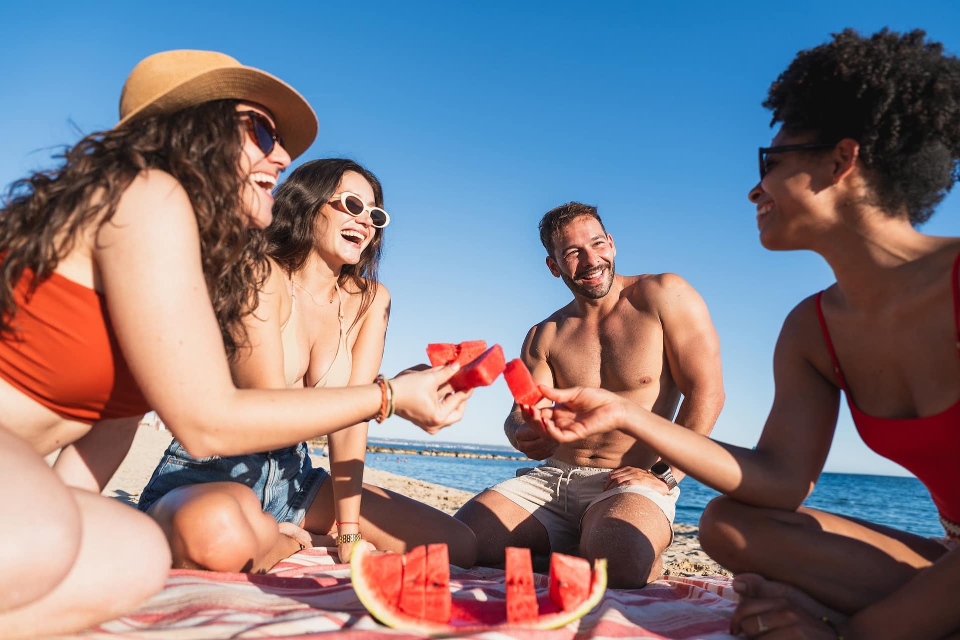 Vier Freunde essen eine Wassermelone am Strand
